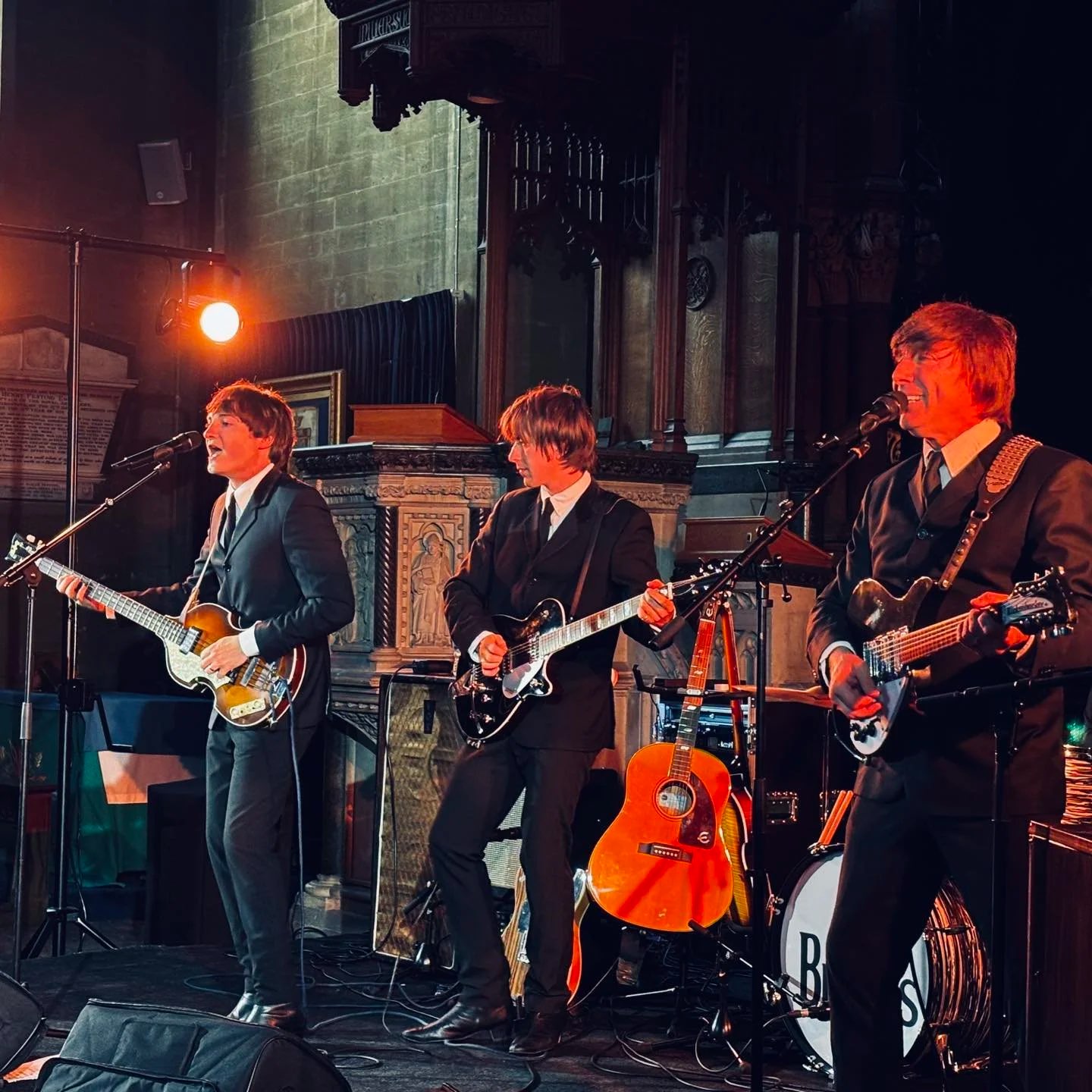 The Beatles Experience performing live with guitars and vocals under warm stage lighting